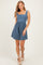 woman wearing a blue smocked mini dress with wide straps and a flared skirt, on a light background