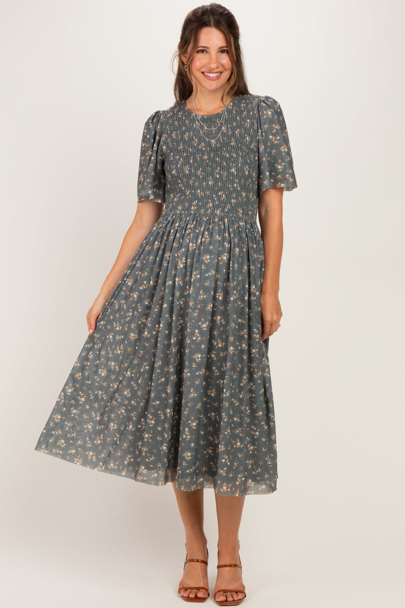 woman wearing a grey floral maternity dress with short puff sleeves and a smocked bodice, standing and smiling
