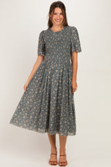 woman wearing a grey floral maternity dress with short puff sleeves and a smocked bodice, standing and smiling