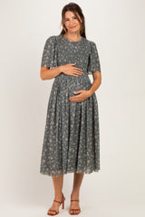 woman wearing a floral print maternity dress with short sleeves and a pleated skirt, holding her baby bump