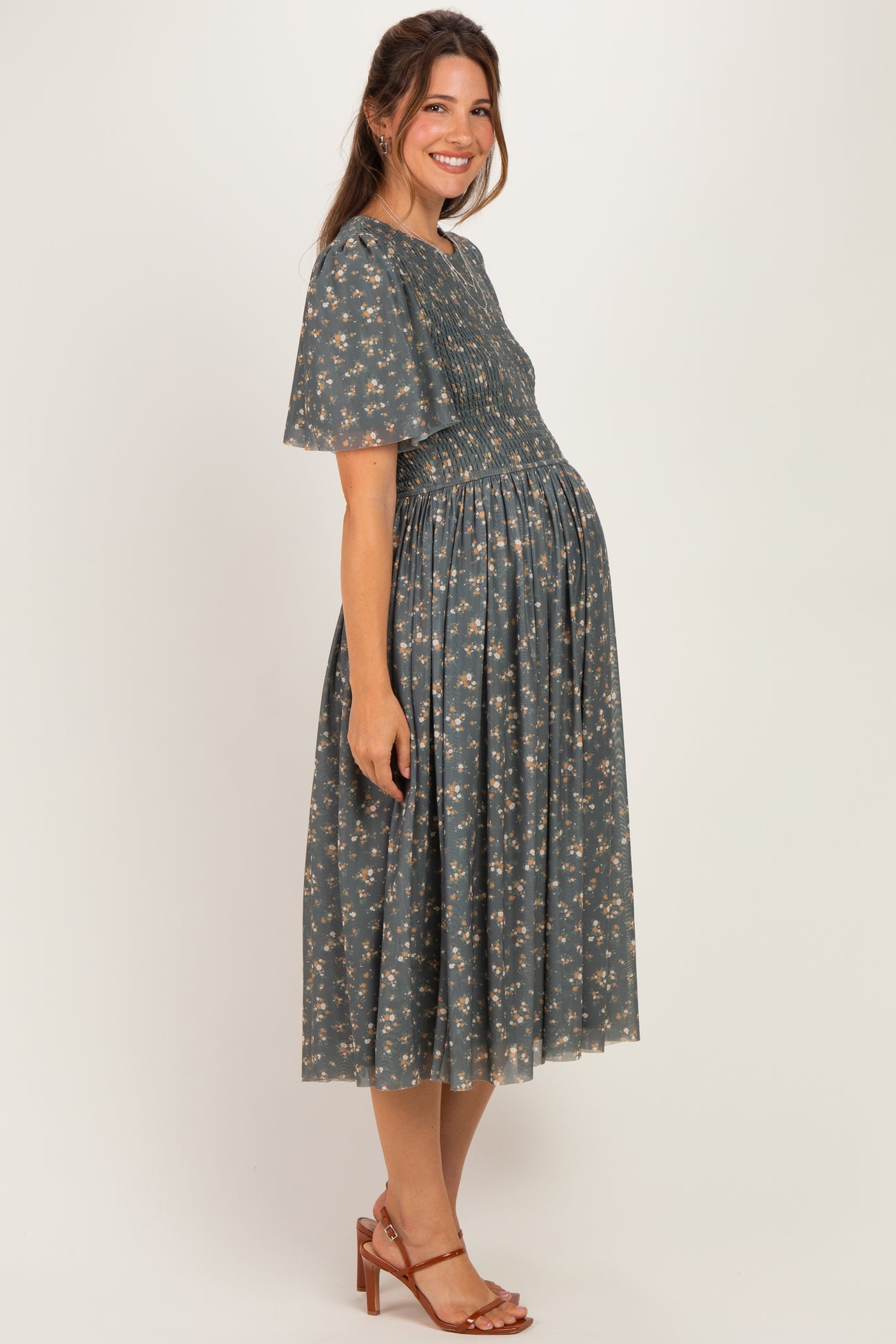 woman wearing a floral maternity dress with short sleeves and a smocked bodice, showcasing her baby bump