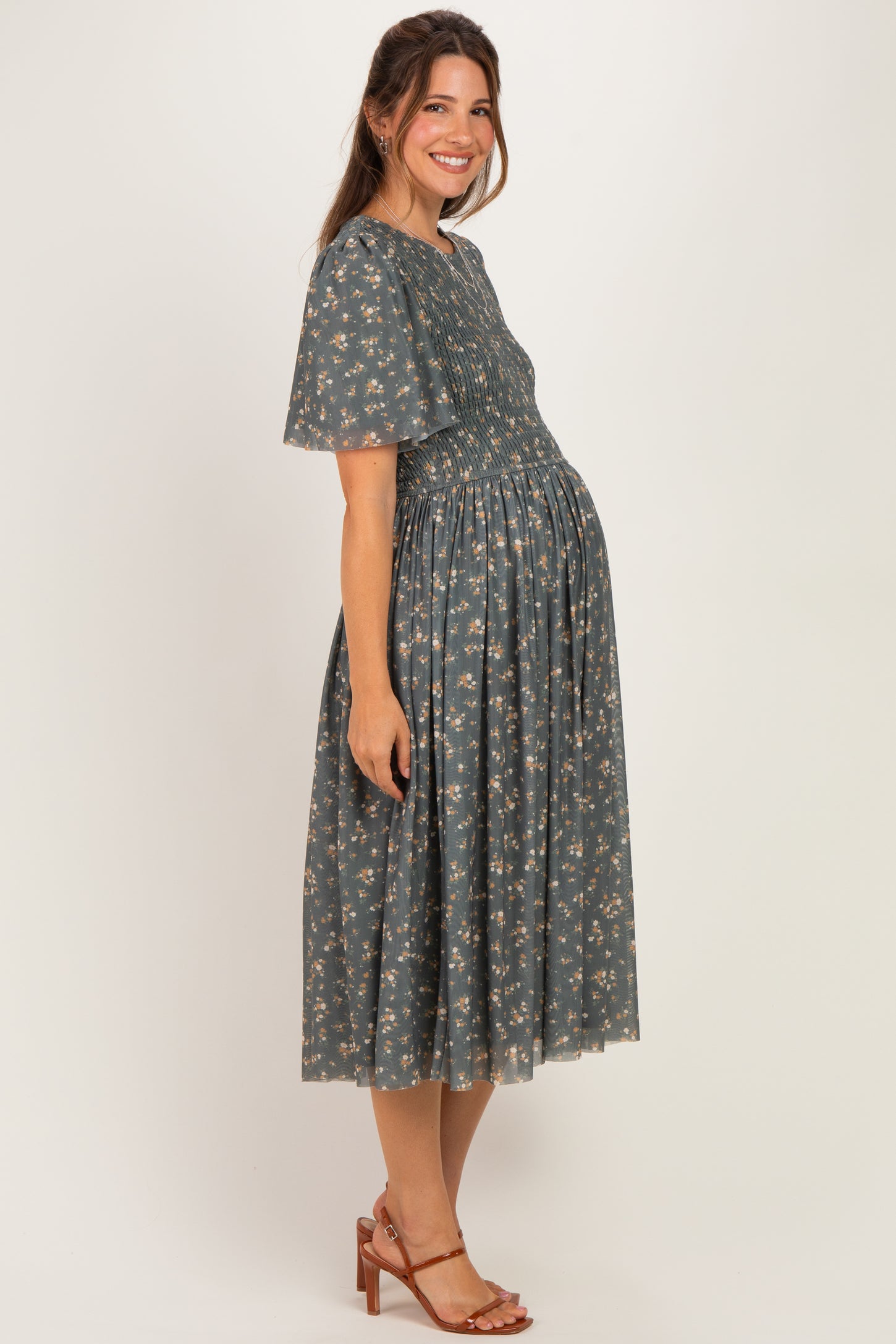 woman wearing a floral maternity dress with short sleeves and a smocked bodice, showcasing her baby bump