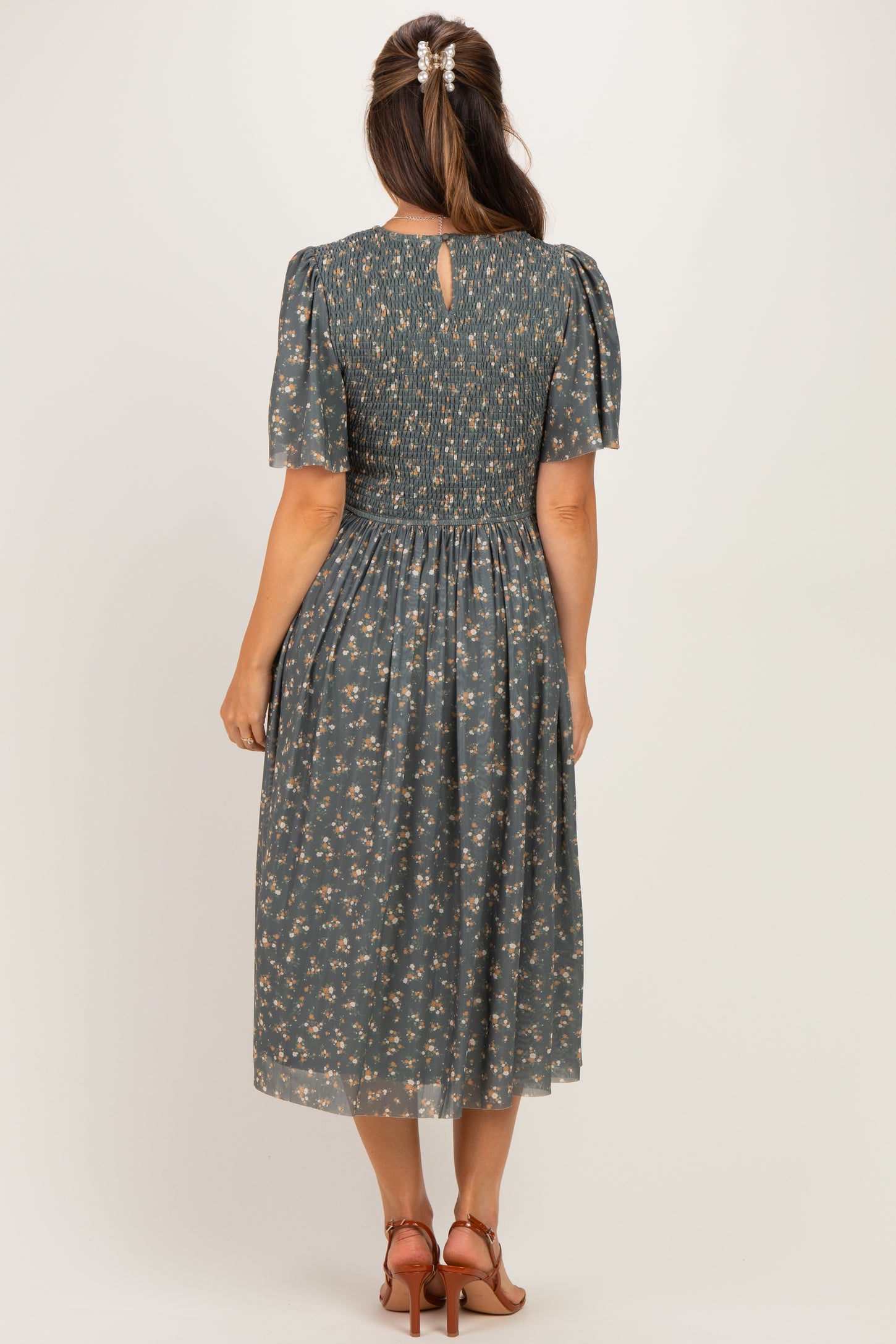 woman wearing a dark green floral maternity dress with short puff sleeves and a smocked back detail