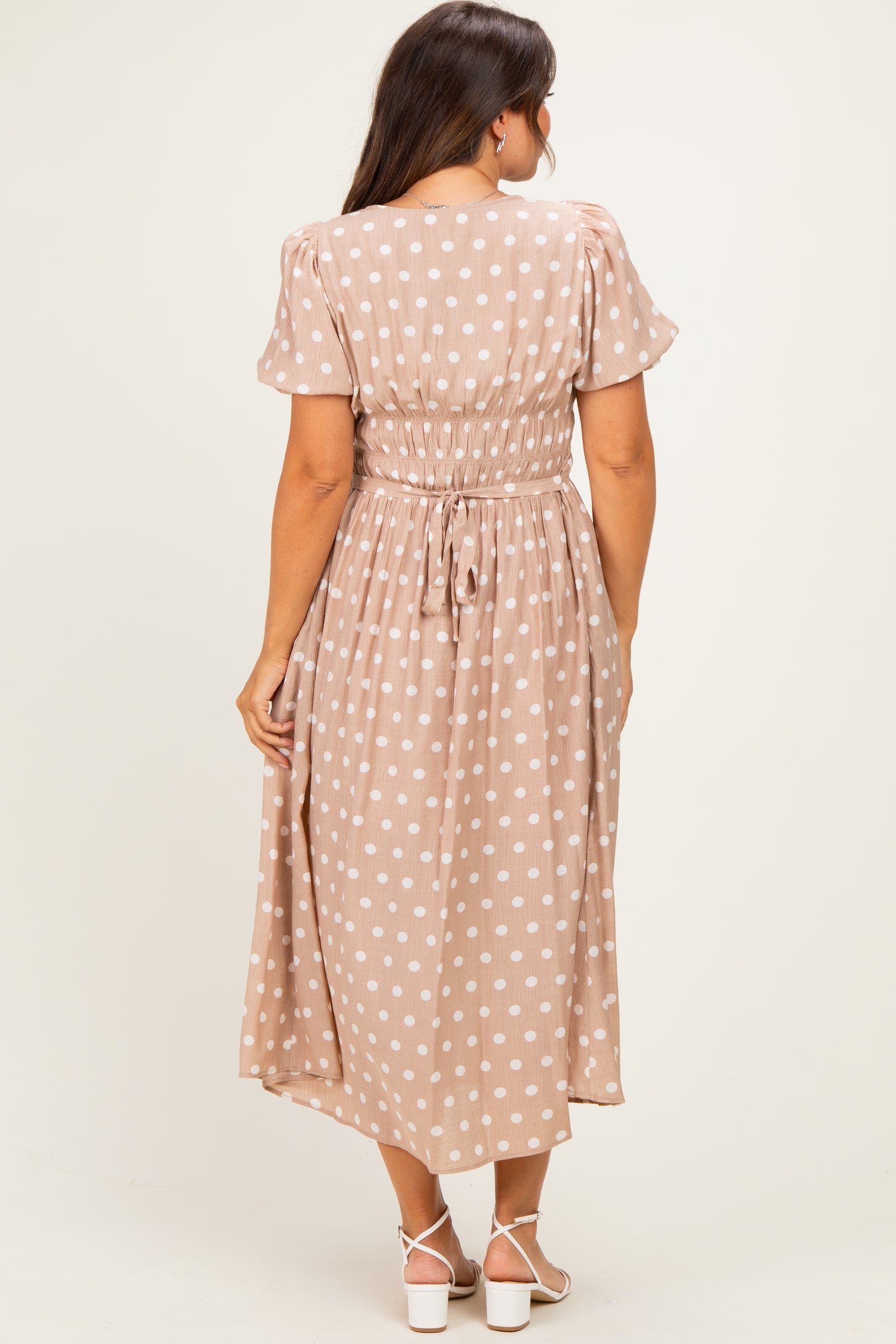 woman wearing a beige maternity dress with white polka dots and a smocked waist, viewed from the back