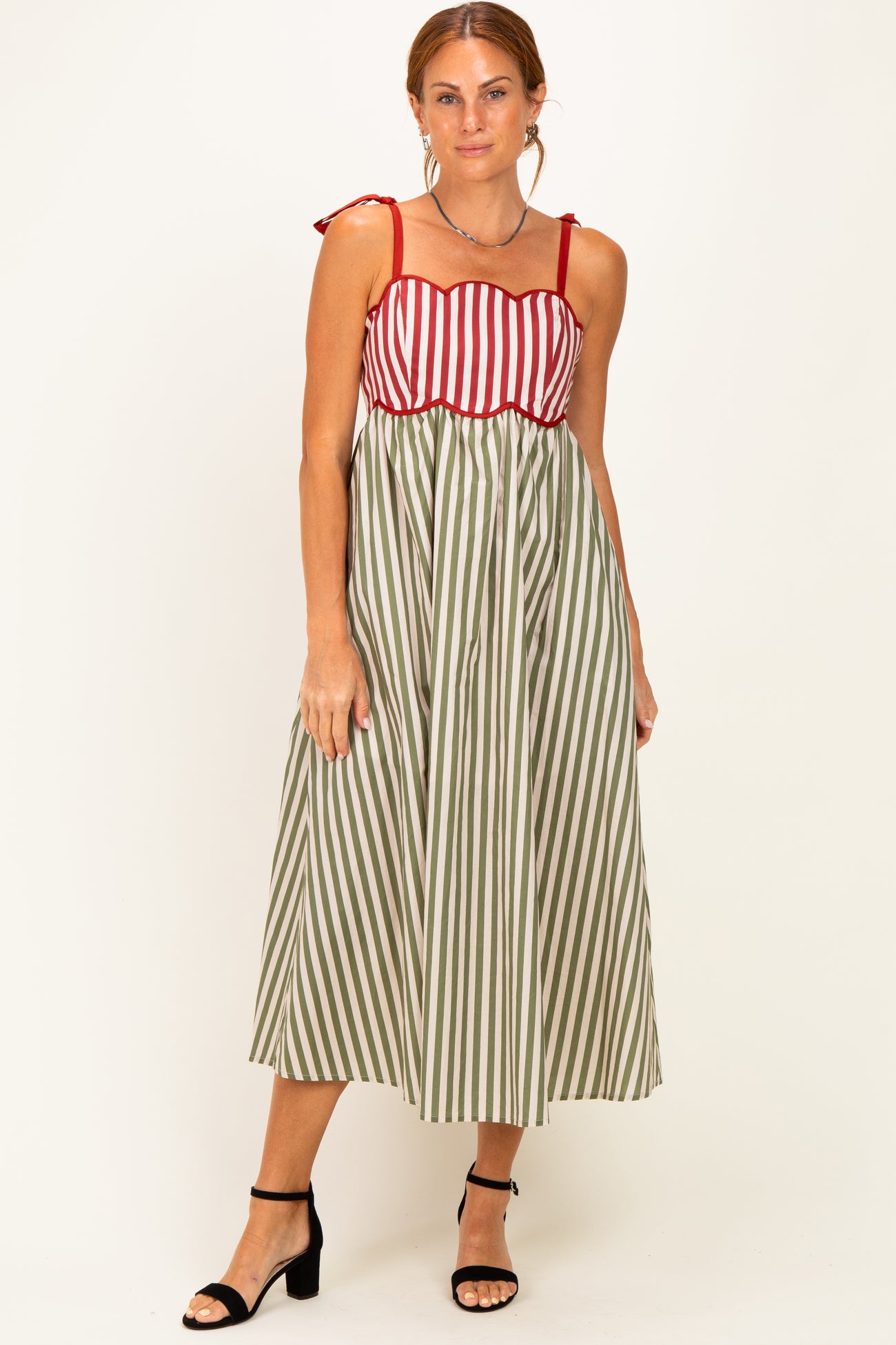 woman wearing a midi dress with red and white striped top and green and white striped skirt, styled with black heels