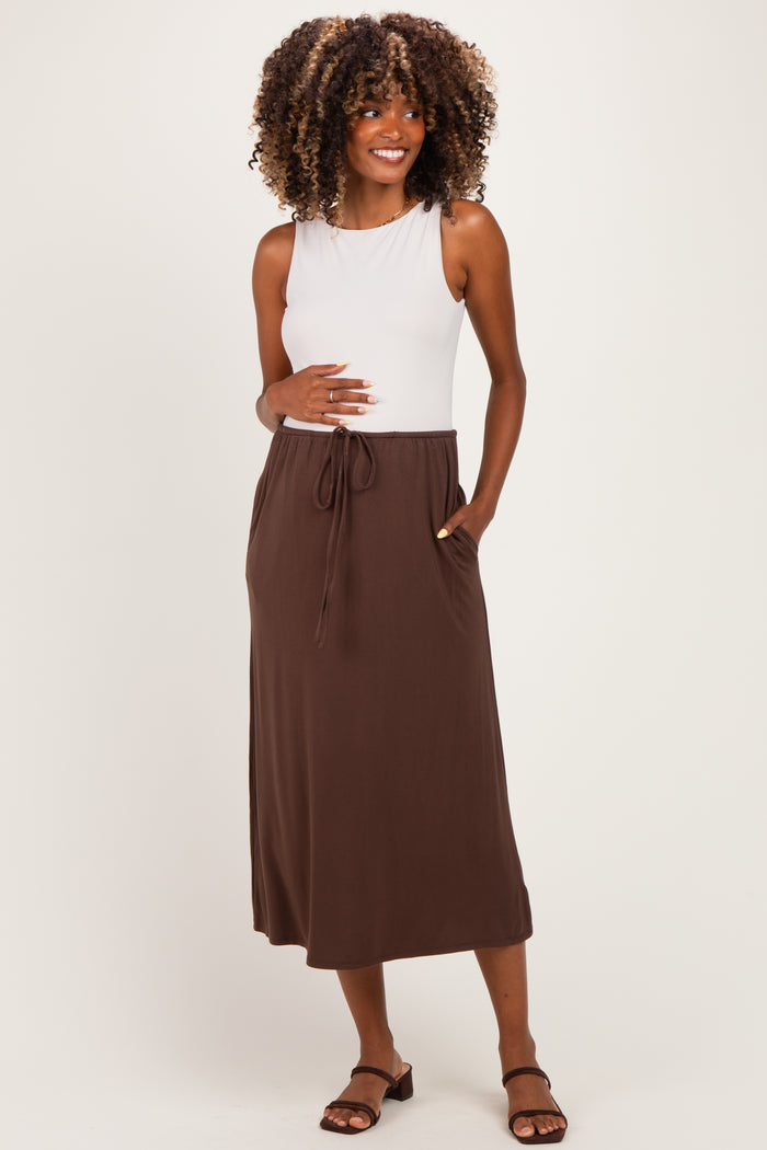 woman wearing a white sleeveless maternity top and a brown maxi skirt with a drawstring, showcasing her baby bump