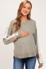 woman wearing a green and beige long sleeve maternity sweater and holding her baby bump