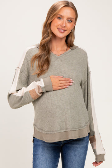 woman wearing a green and beige long sleeve maternity sweater and holding her baby bump