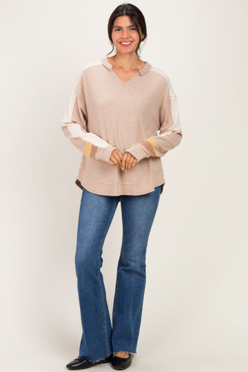 woman wearing a beige oversized long sleeve sweater with color block details and flared jeans