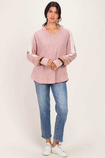 woman wearing a pink oversized hoodie with contrasting sleeves and light blue jeans, standing on a neutral background