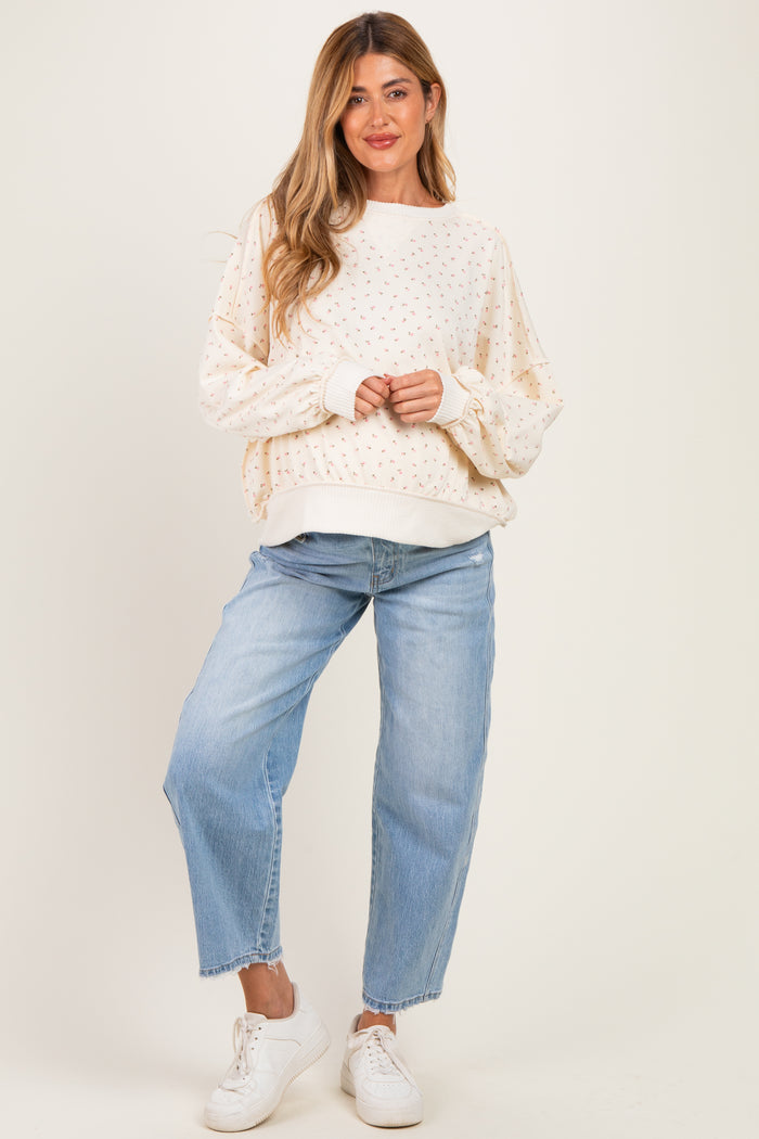 woman wearing a cream maternity sweatshirt with floral print and puff sleeves, paired with light blue jeans and white sneakers