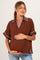woman wearing a brown maternity top with blue trim, holding her baby bump and smiling