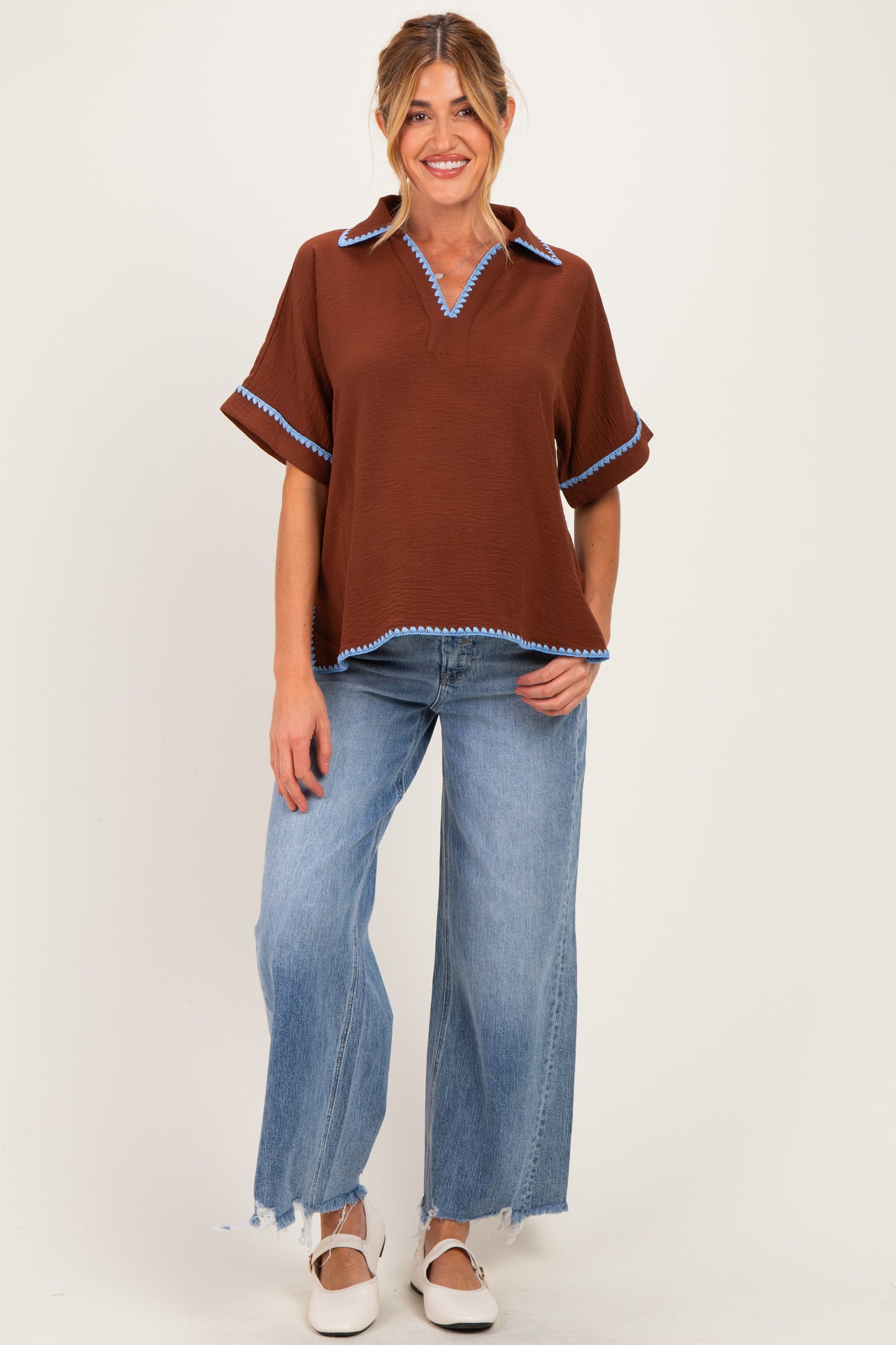 woman wearing a brown maternity top with blue trim and a relaxed fit, paired with light wash wide leg jeans