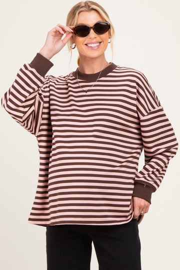 woman wearing a brown and pink striped maternity top with oversized fit and long sleeves, holding sunglasses and showing baby bump