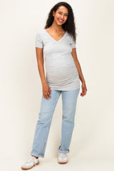 woman wearing a grey v-neck maternity top with a visible baby bump and light blue jeans