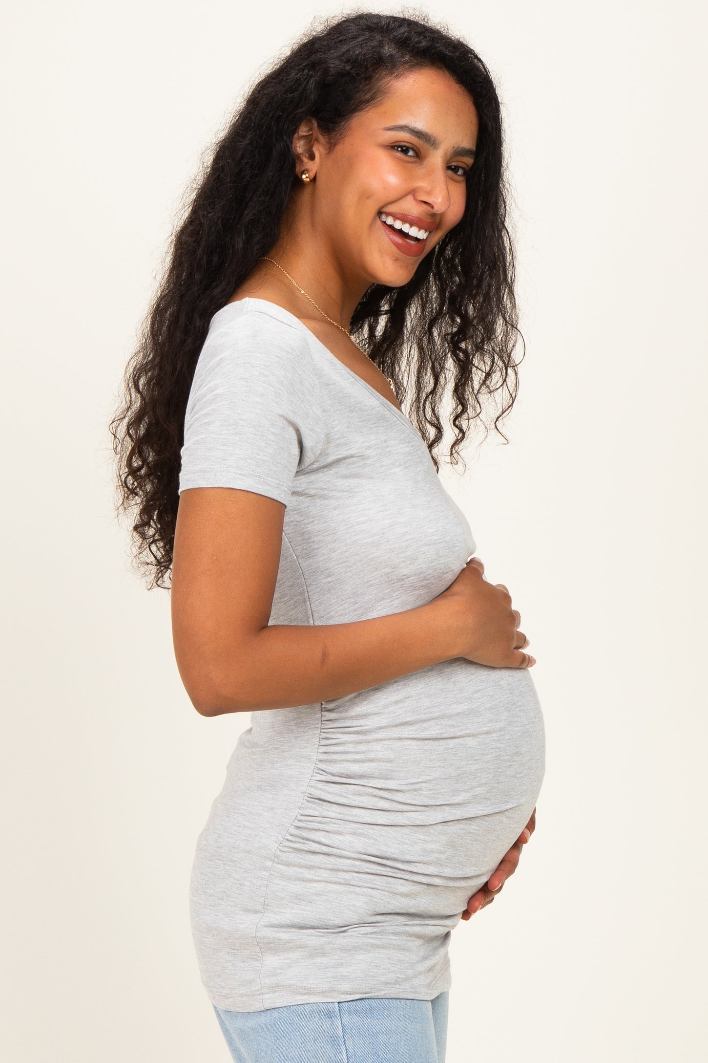 woman wearing a gray short sleeve maternity top and holding her baby bump