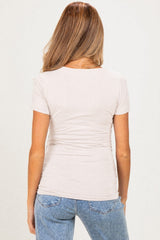 woman wearing a beige short sleeve maternity top with a fitted silhouette and back ruching, paired with jeans