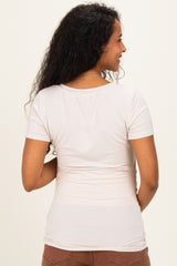 woman wearing a light beige short sleeve maternity top, showing a fitted style from the back