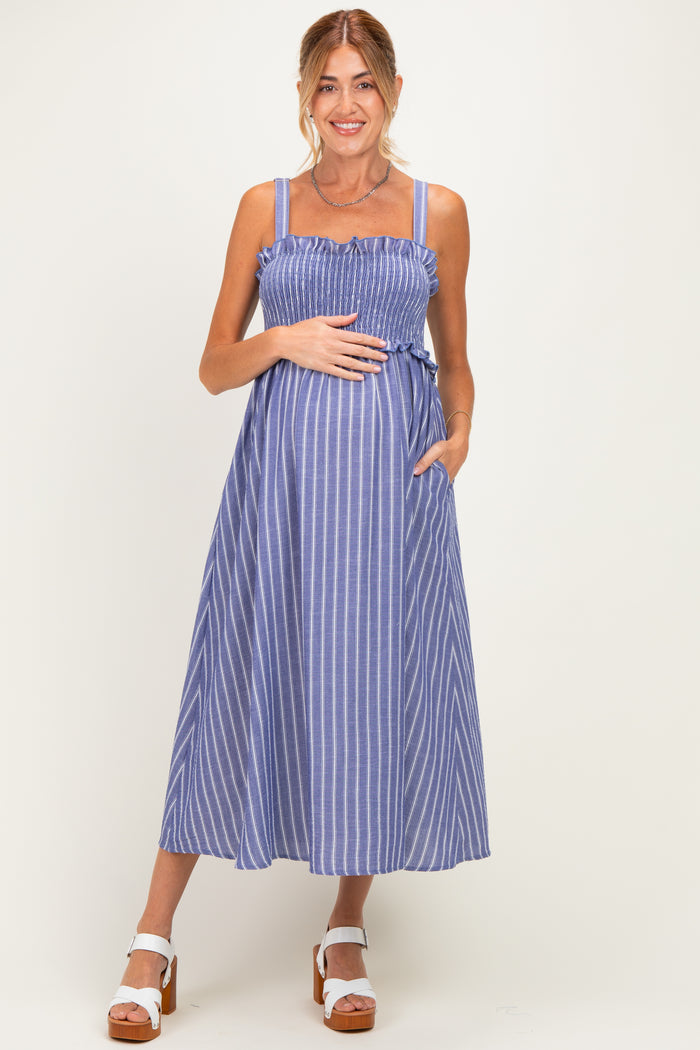 woman wearing a blue and white striped maternity dress with smocked bodice and pockets, holding her baby bump