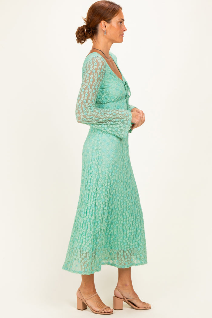 woman wearing a mint green lace dress with long sleeves and a flared skirt, standing in profile