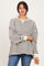 woman wearing a gray and white striped oversized sweater with side slits and long sleeves, paired with blue jeans