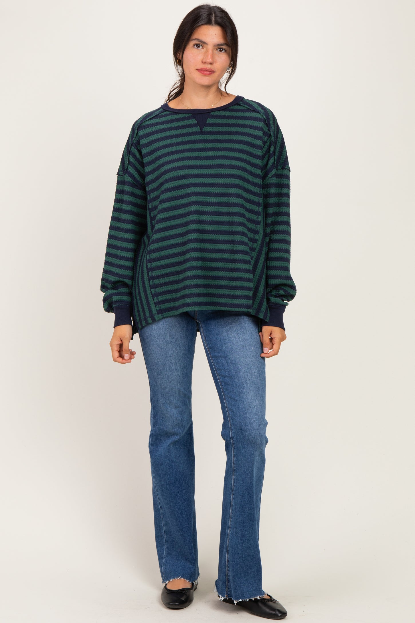 woman wearing a navy and green striped oversized sweatshirt with a crew neck and long sleeves, paired with flared jeans