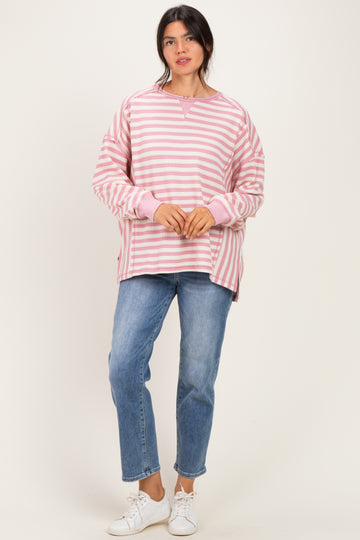 woman wearing a pink and white striped oversized sweatshirt with side slits and light blue jeans