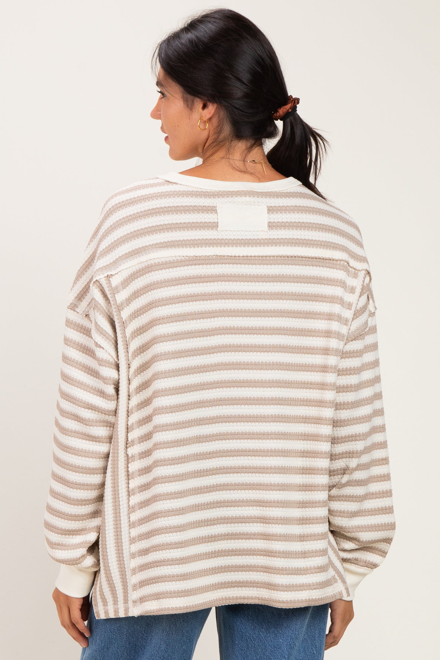 woman wearing a beige and cream striped oversized sweater, showing the back view with relaxed fit and long sleeves