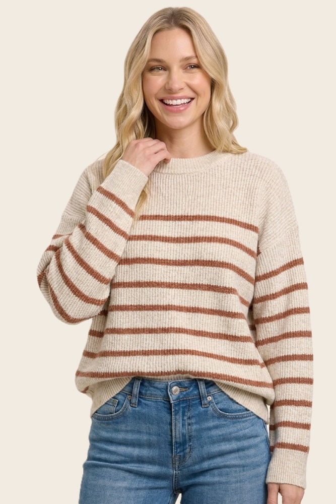 woman wearing a cream striped sweater with brown stripes and blue jeans, smiling and touching her neck