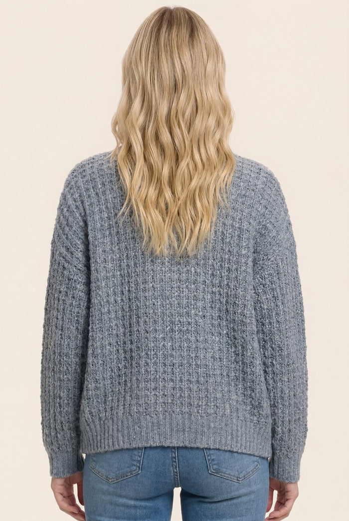 back view of a woman wearing a cozy grey textured sweater with a relaxed fit and ribbed detailing