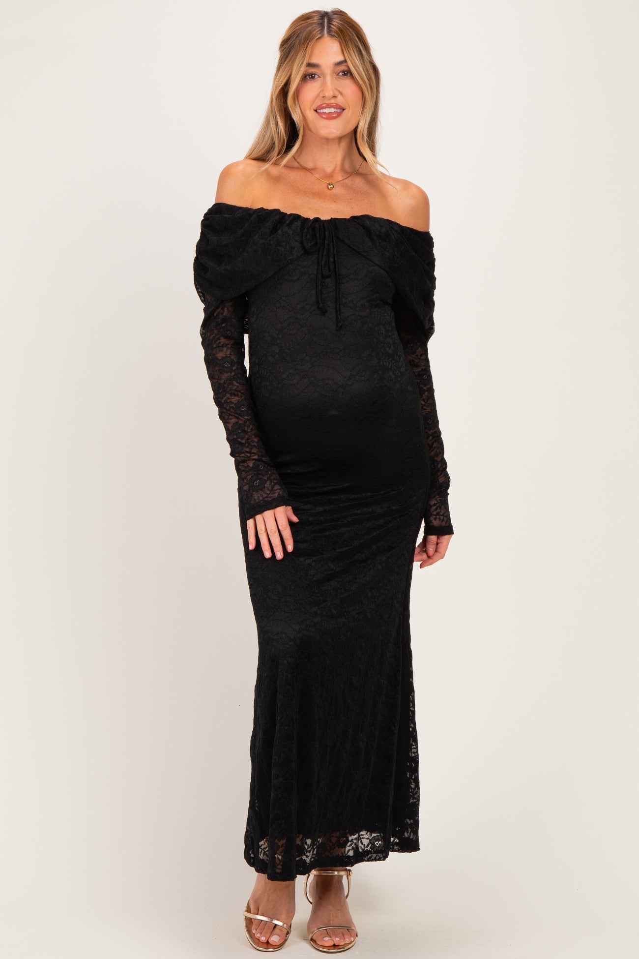 woman wearing a black off-the-shoulder lace maternity dress with long sleeves and a fitted silhouette, showing her baby bump