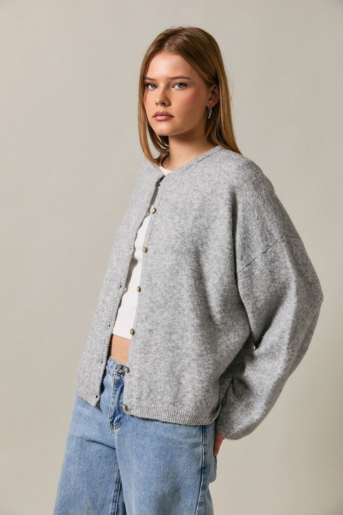 woman wearing a gray oversized cardigan with buttons and loose sleeves, paired with a white top and blue jeans