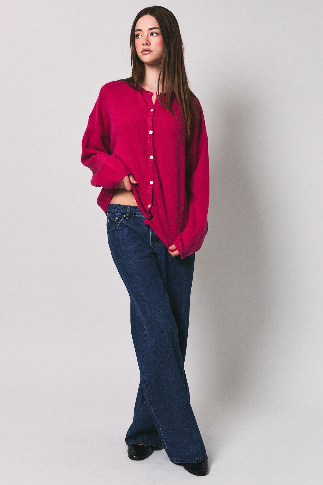 woman wearing a fuchsia oversized cardigan with button details and wide-leg jeans