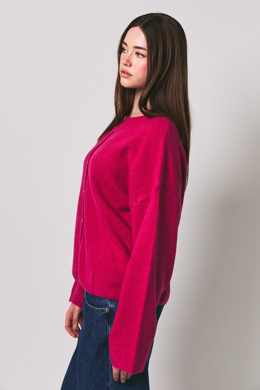 woman wearing a bright pink oversized sweater with wide sleeves and paired with denim jeans