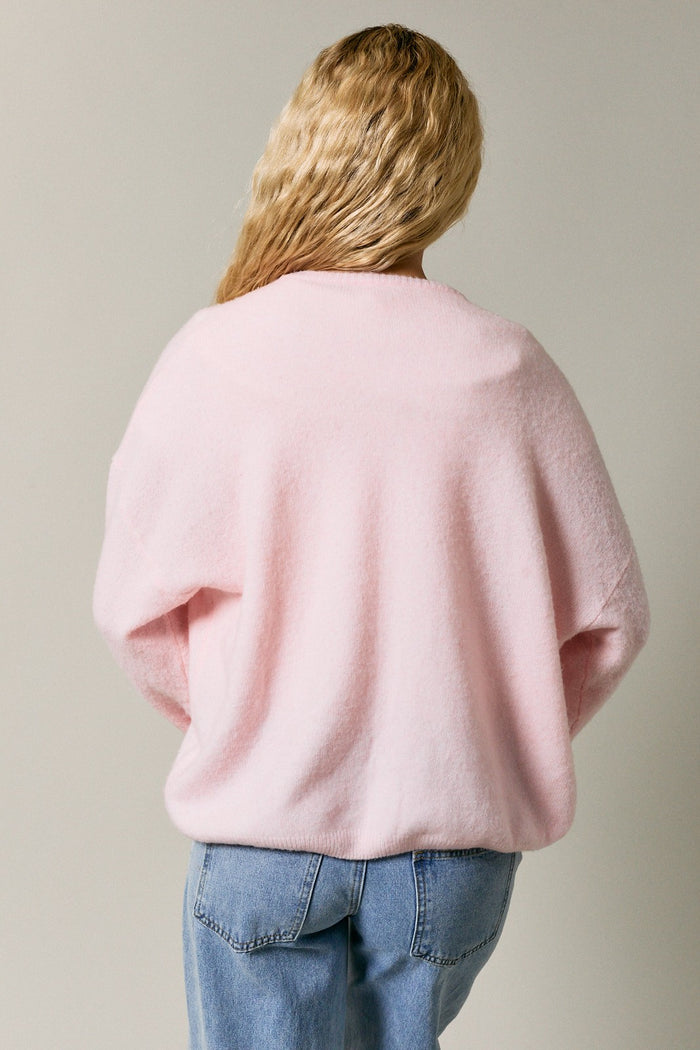 woman wearing a light pink oversized sweater, seen from the back, paired with blue jeans