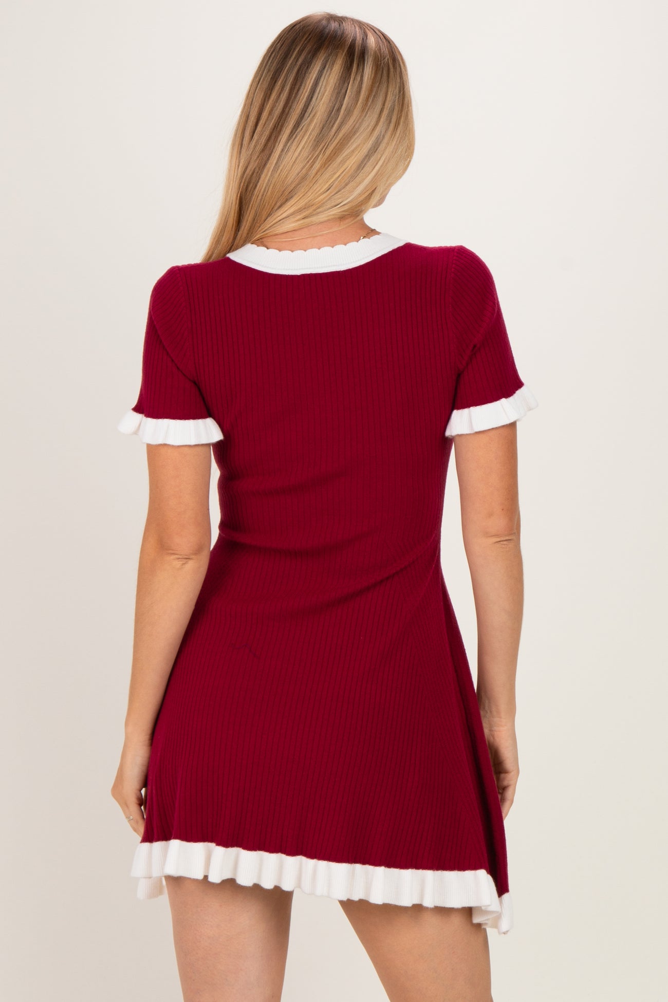 woman wearing a red ribbed dress with white ruffle details on the sleeves and hem, shown from the back
