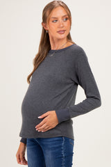 woman wearing a dark grey long sleeve maternity top with a visible baby bump and blue jeans