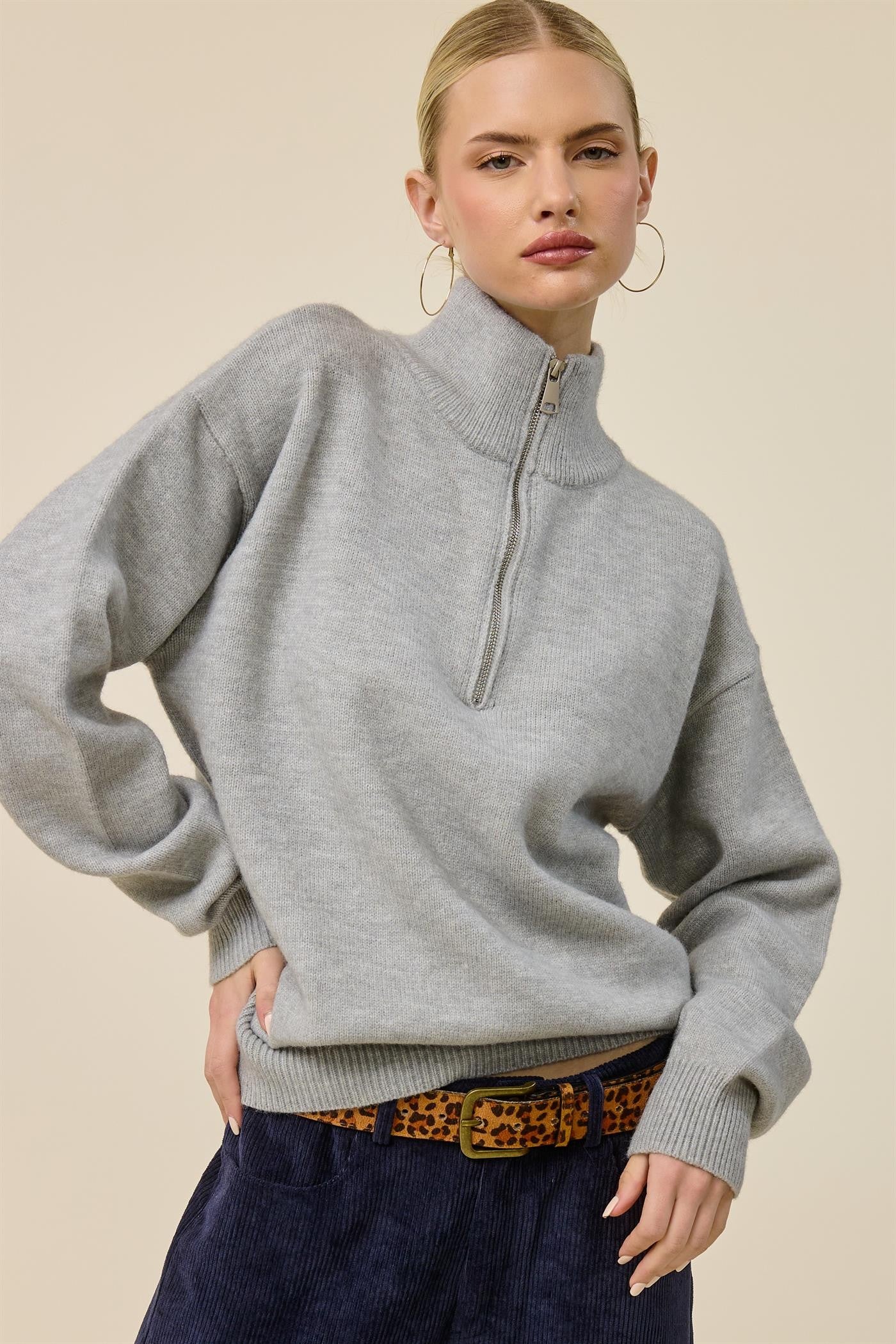 woman wearing a gray half-zip sweater paired with a leopard print belt and navy corduroy pants