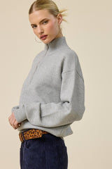 woman wearing a gray half-zip sweater and a leopard print belt, styled with a confident pose