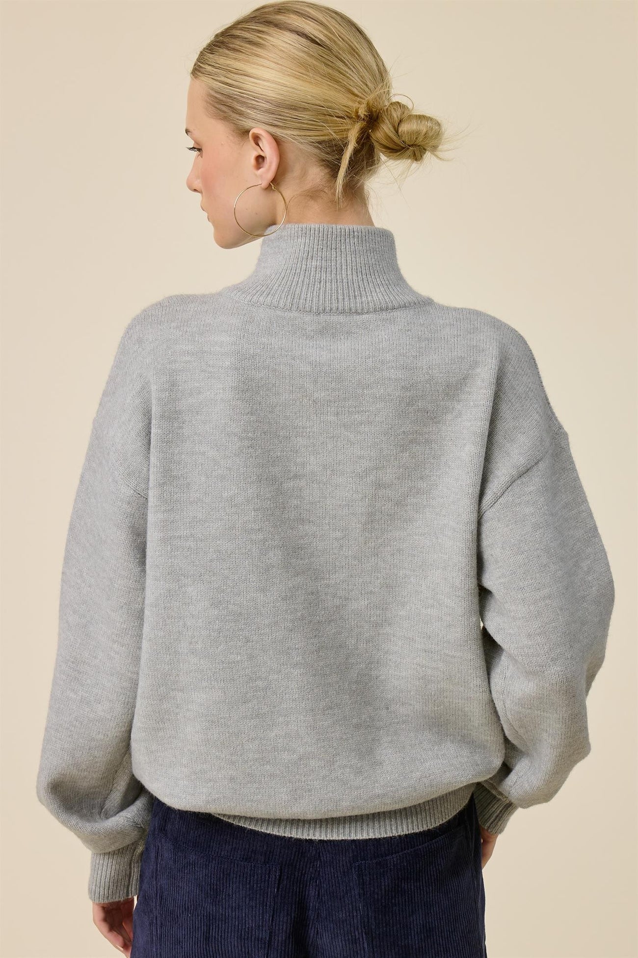 woman wearing a gray oversized turtleneck sweater with balloon sleeves, viewed from the back