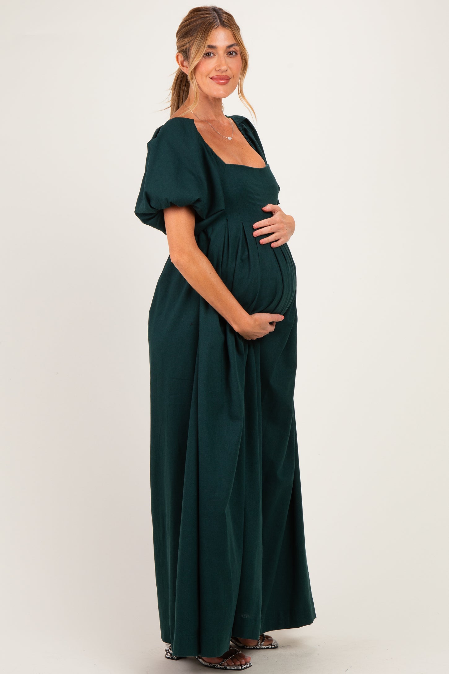woman wearing a dark green short sleeve maternity dress holding her baby bump