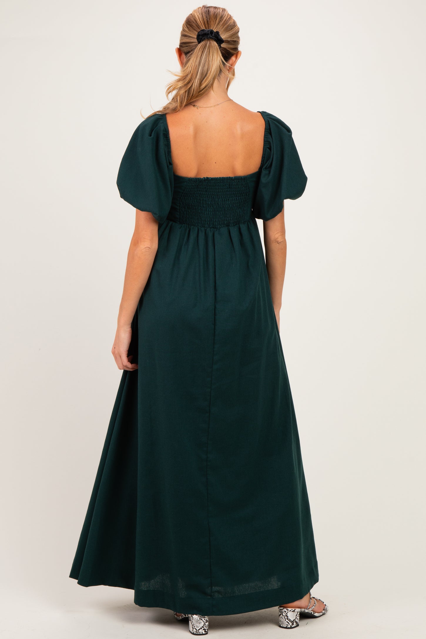woman wearing a dark green maternity maxi dress with puff sleeves and a smocked back, showing her baby bump
