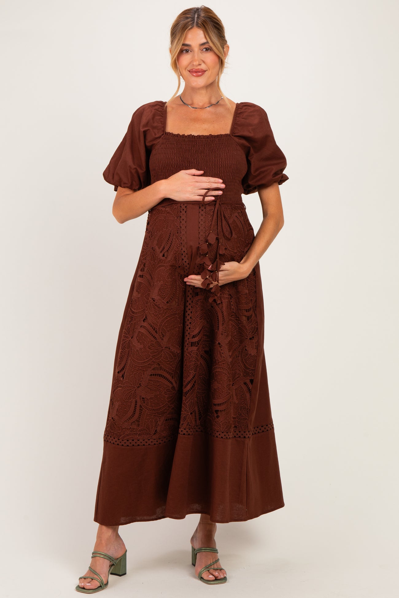 woman wearing a brown maternity dress with puff sleeves and embroidery, holding her baby bump