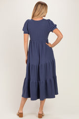 woman wearing a navy blue tiered midi dress with puff sleeves, showing the back view and styled with sandals