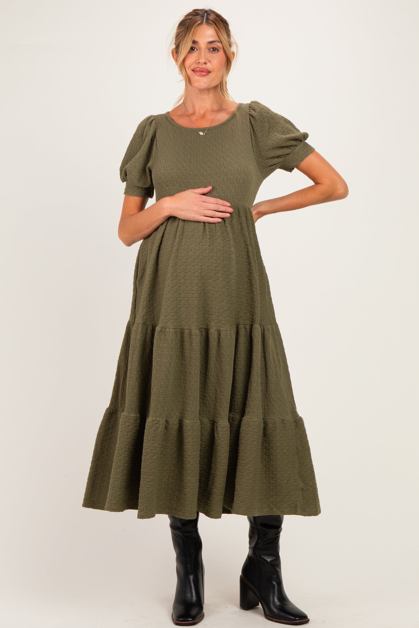 woman wearing an olive green maternity dress with puff sleeves and a tiered skirt, holding her baby bump