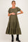 woman wearing an olive green maternity dress with puff sleeves and a tiered skirt, holding her baby bump