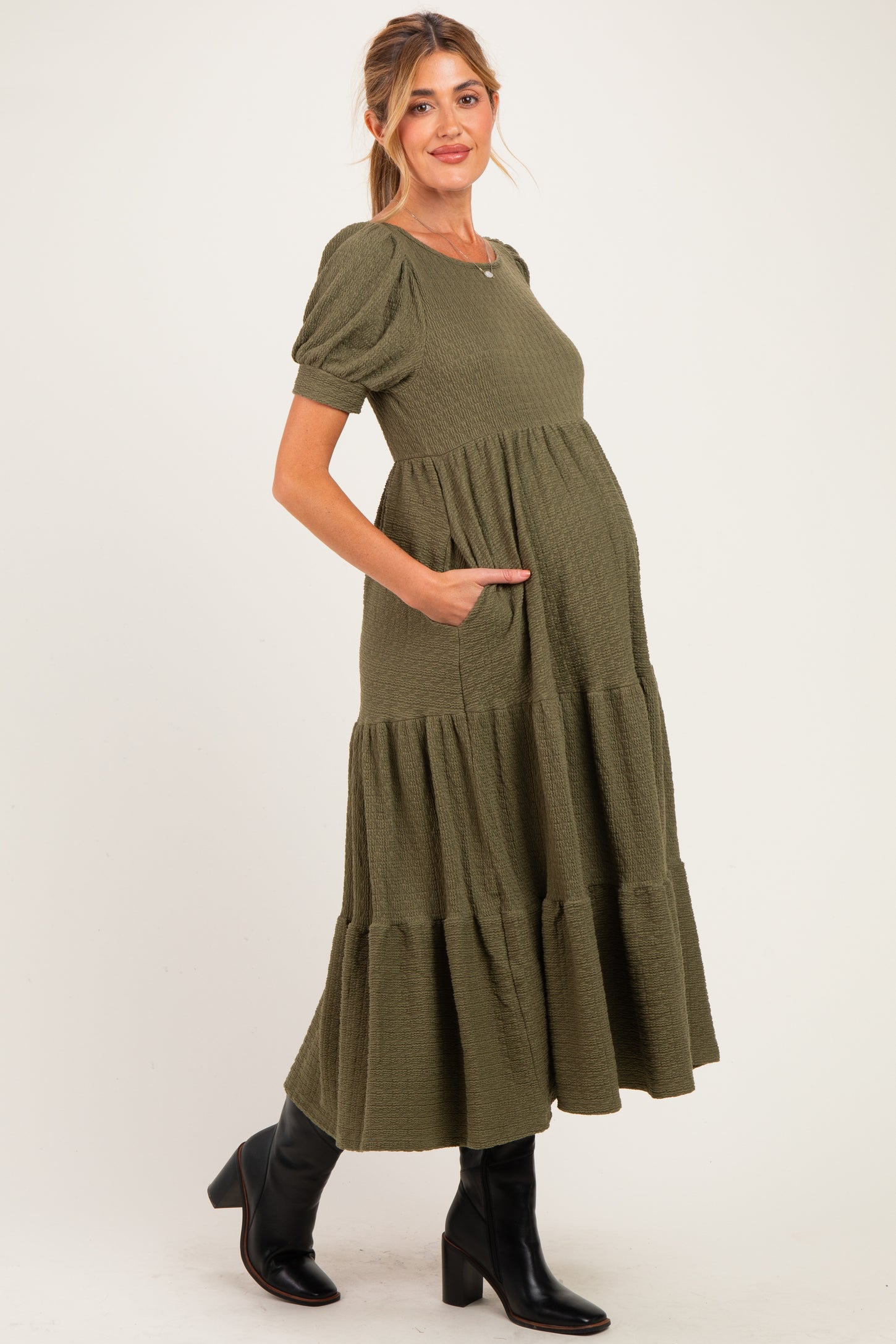 woman wearing a dark olive green maternity tiered maxi dress with short puff sleeves and pockets, showing her baby bump