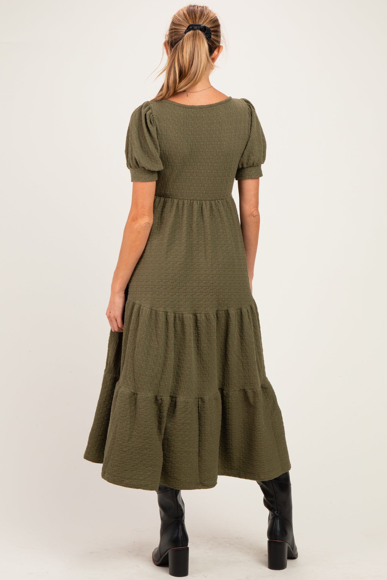 woman wearing a dark green maternity midi dress with puff sleeves and a tiered skirt, showing her baby bump