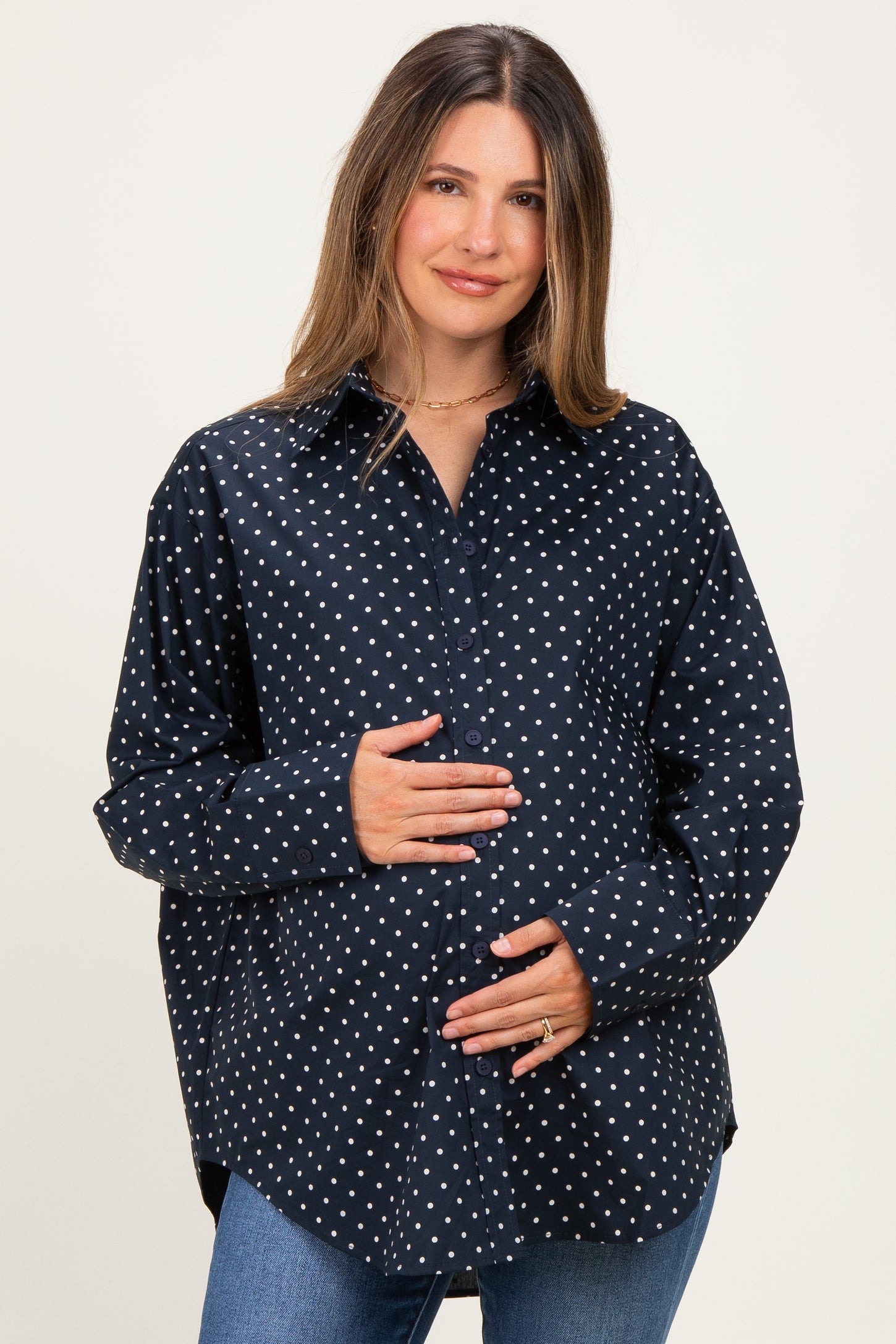 woman wearing a navy blue polka dot maternity shirt and holding her baby bump