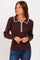 woman wearing a brown ribbed sweater with white pom-pom trim and a collared neckline, standing and looking to the side